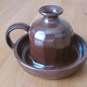 May include: A brown ceramic butter dish with a lid and a handle. The dish has a glazed finish and a slightly textured surface.
