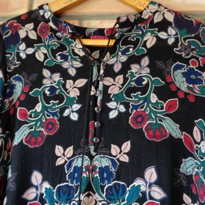 May include: Black long-sleeve shirt with a floral pattern in red, blue, and green. The shirt has a mandarin collar and a button-down placket. The brand name "INDISKA" is visible on the wooden hanger.