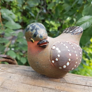May include: A ceramic bird figurine with brown, white, and black speckled paint. The bird has a round body with white dots and a black beak.