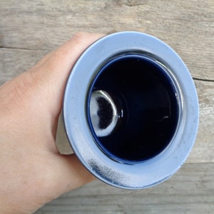 May include: A blue ceramic cup with a white rim. The cup is empty and the inside is visible.