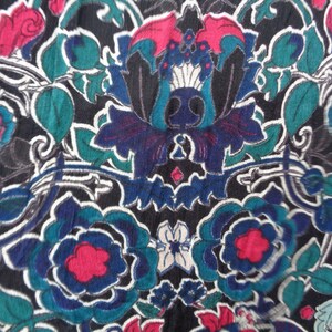 May include: Close-up of a fabric with a floral pattern. The design features large, stylized flowers in shades of blue, teal, and red against a black background. White outlines define the floral shapes, creating a vintage aesthetic.