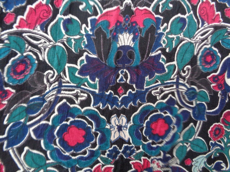 May include: Close-up of a fabric with a floral pattern. The design features large, stylized flowers in shades of blue, teal, and red against a black background. White outlines define the floral shapes, creating a vintage aesthetic.