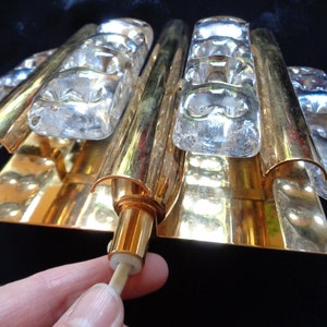 K&ouml;nnte beinhalten: Goldene Wandleuchte mit klaren Glaspaneelen. Die Leuchte hat ein modernes Design und ist perfekt, um jedem Raum einen Hauch von Eleganz zu verleihen.