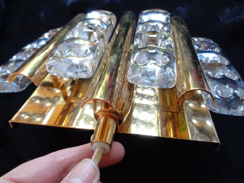 K&ouml;nnte beinhalten: Goldene Wandleuchte mit klaren Glaspaneelen. Die Leuchte hat ein modernes Design und ist perfekt, um jedem Raum einen Hauch von Eleganz zu verleihen.