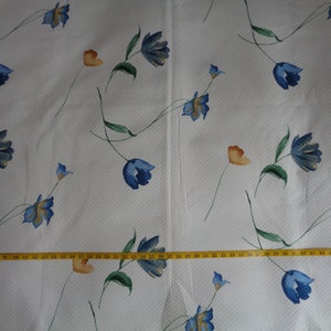 May include: White fabric with a repeating pattern of blue and orange flowers. The fabric is textured and has a subtle sheen.