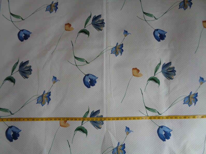 May include: White fabric with a repeating pattern of blue and orange flowers. The fabric is textured and has a subtle sheen.
