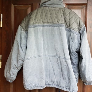 May include: A blue and grey quilted jacket with a zip closure. The jacket has a diamond pattern on the upper back and a solid colour on the lower back.