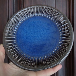 May include: A blue ceramic plate with a dark brown rim and a textured design. The plate has a slightly raised edge and a smooth, glossy finish.