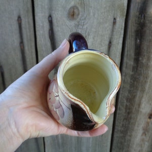 May include: A brown and cream ceramic pitcher with a floral design. The pitcher has a handle and a spout.