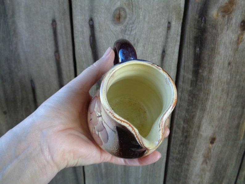 May include: A brown and cream ceramic pitcher with a floral design. The pitcher has a handle and a spout.