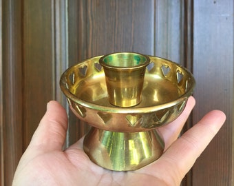 以下が含まれることがあります： ハート型のデザインの金色の金属製のキャンドルホルダー。ホルダーは丸いベースと単一のキャンドルカップを持っています。