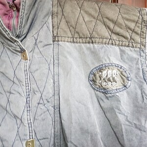 May include: A blue quilted jacket with a brown quilted patch on the shoulder. The jacket has a zip fastening and a button on the front. The jacket has a logo patch on the right sleeve that says "Pepe Jeans London".