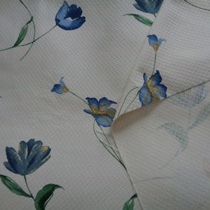May include: White fabric with a blue and yellow floral pattern. The fabric has a textured surface and the flowers are stylized.