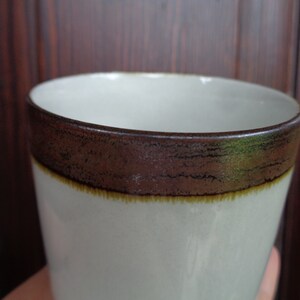 Puede incluir: Una taza de cer&aacute;mica blanca con una banda marr&oacute;n alrededor del borde y una fina banda amarilla debajo. La taza tiene una superficie ligeramente texturizada y un dise&ntilde;o simple y elegante. Adecuada para bebidas fr&iacute;as o calientes.