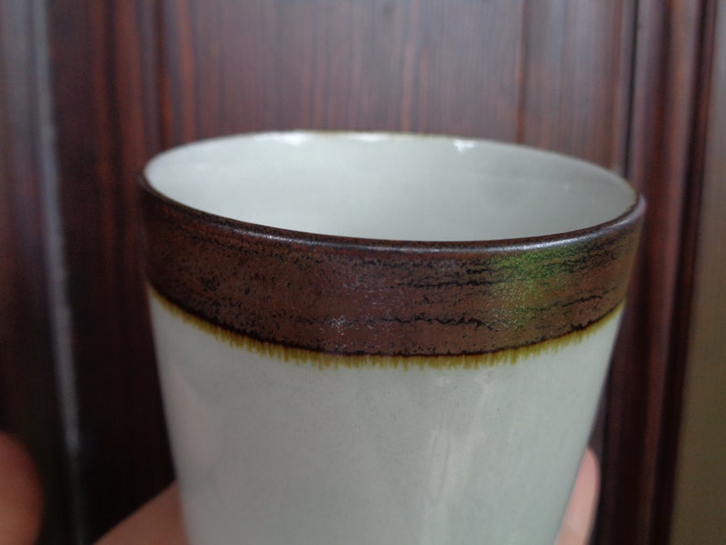 Puede incluir: Una taza de cer&aacute;mica blanca con una banda marr&oacute;n alrededor del borde y una fina banda amarilla debajo. La taza tiene una superficie ligeramente texturizada y un dise&ntilde;o simple y elegante. Adecuada para bebidas fr&iacute;as o calientes.