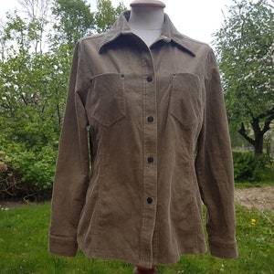 May include: A brown corduroy shirt with a button-up front and two chest pockets. The shirt has long sleeves and a collared neckline.