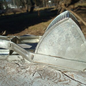 May include: A vintage, silver potato ricer. The kitchen utensil has a triangular head with a perforated surface and long handles for pressing. The ricer is made of metal and shows signs of wear, suggesting it is an antique kitchen tool.