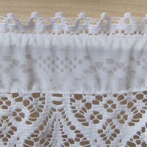 May include: White lace curtain valance with a delicate floral pattern. The valance has a scalloped top edge and a straight bottom edge.