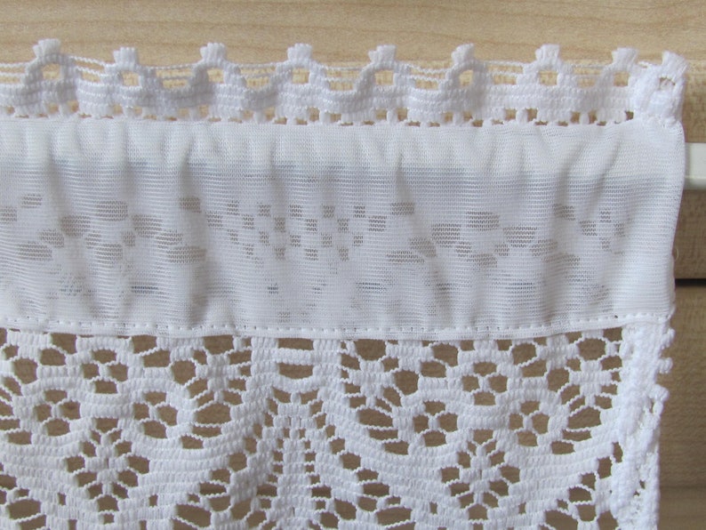 May include: White lace curtain valance with a delicate floral pattern. The valance has a scalloped top edge and a straight bottom edge.