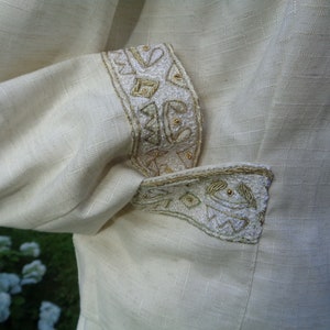 May include: A white linen jacket with gold embroidery on the cuffs and pocket flap.