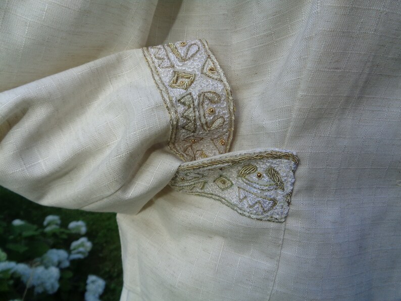 May include: A white linen jacket with gold embroidery on the cuffs and pocket flap.