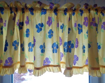 May include: Yellow valance with a ruffled bottom and a floral pattern of blue and purple flowers.