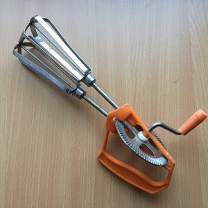 Mid Century kitchen tool, manual mixer. Stainless steel egg beater with orange plastic handles