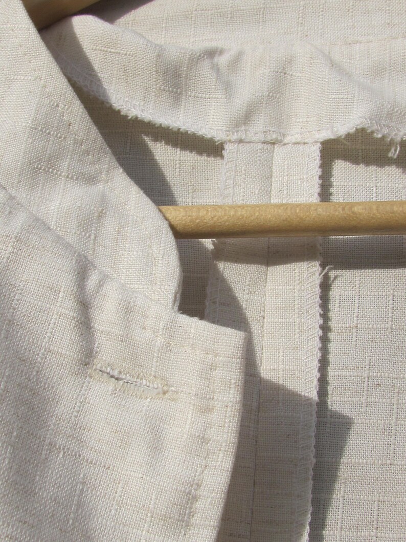 May include: A close-up of a white linen fabric with a seam down the center. The fabric is folded over and has a wooden hanger on top.