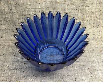 May include: A cobalt blue glass bowl with a unique petal-like design. The bowl is made of thick glass and has a smooth, rounded interior.