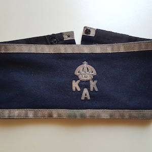 May include: A dark blue fabric band with a silver embroidered crown and the letters "K.K.A."