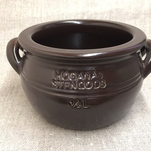 Könnte beinhalten: Eine dunkelbraune Keramikschüssel mit zwei Griffen. Die Schüssel trägt den geprägten Text "HÖGANÄS STENGODS" und "½ L". Die Schüssel ist dunkelbraun und scheint aus Steinzeug zu sein.