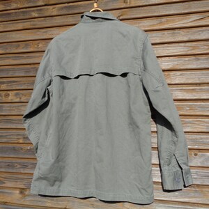 Puede incluir: Una camisa de manga larga de color verde claro con botones y un bolsillo con solapa en la espalda.