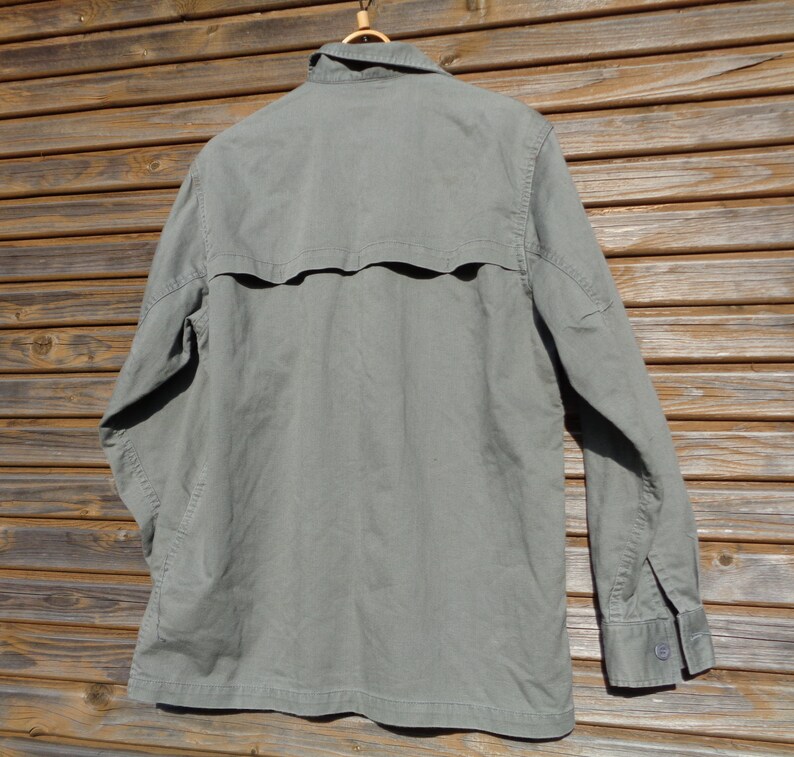 Puede incluir: Una camisa de manga larga de color verde claro con botones y un bolsillo con solapa en la espalda.