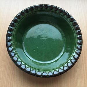 May include: A green ceramic bowl with a dark brown rim decorated with a repeating heart pattern.