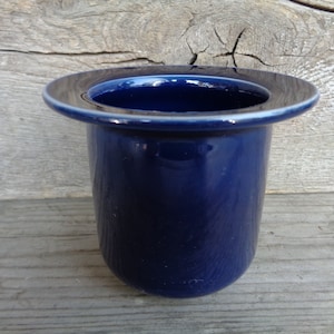 May include: A dark blue ceramic toothbrush holder with a wide rim.