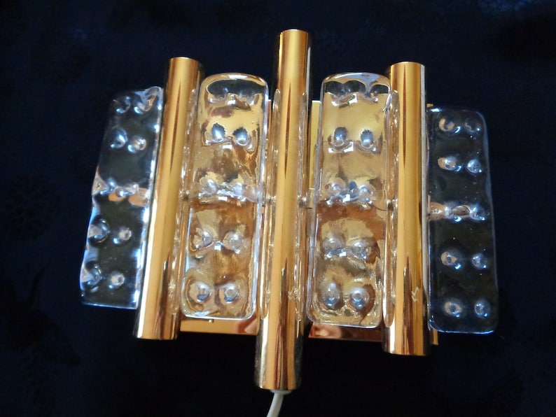 K&ouml;nnte beinhalten: Goldene Wandleuchte mit klaren Glasplatten. Die Glasplatten haben eine strukturierte Oberfl&auml;che mit kleinen Blasen.