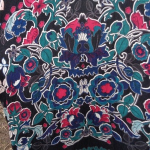 May include: Black fabric with a vibrant floral pattern. The design features large, stylized flowers in shades of blue, red, and teal, set against a dark background. The pattern includes intricate leaf and vine details.