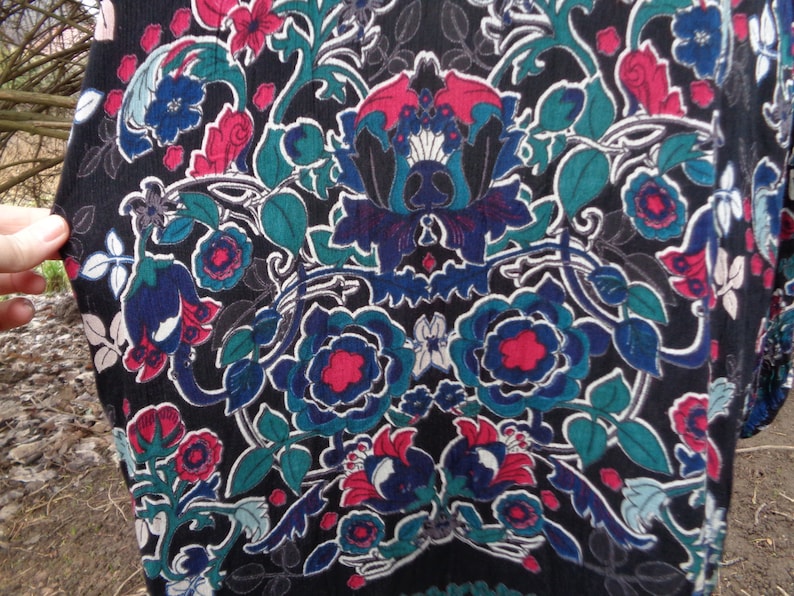 May include: Black fabric with a vibrant floral pattern. The design features large, stylized flowers in shades of blue, red, and teal, set against a dark background. The pattern includes intricate leaf and vine details.