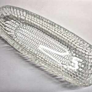 May include: A clear, oblong glass dish with a textured, honeycomb-like pattern. The dish has a slightly raised rim and a smooth, rectangular interior. The glass reflects light, creating highlights and shadows. This decorative dish is suitable for serving or display.