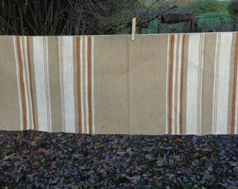 May include: A beige and white striped rug with orange stripes hanging on a clothesline. The rug is made of a woven material and has a rustic look.