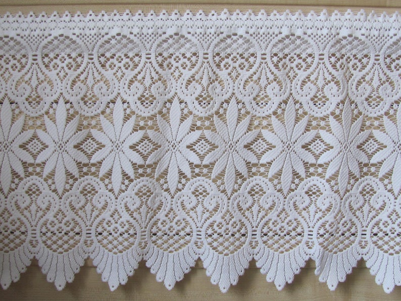 May include: White lace trim with a scalloped edge and a floral pattern. The lace is delicate and intricate, with a repeating design of flowers and leaves.