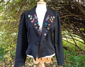 May include: A black blazer with a unique design featuring a variety of colorful buttons and small key-shaped charms arranged in a heart shape on the front.