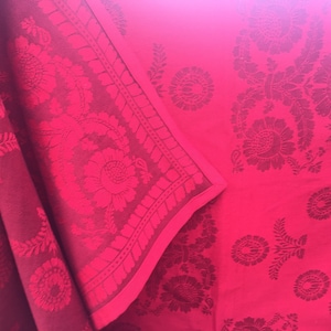 May include: A close-up of a red fabric with a floral pattern. The fabric has a raised texture and a subtle sheen.