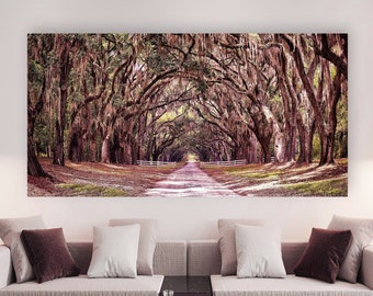 May include: A living room interior design with a large framed photograph of a long, tree-lined road. The photograph is hanging on a white wall above a light gray sofa with brown throw pillows. There is a black coffee table in front of the sofa, and a black floor lamp with a round black shade in the corner of the room.