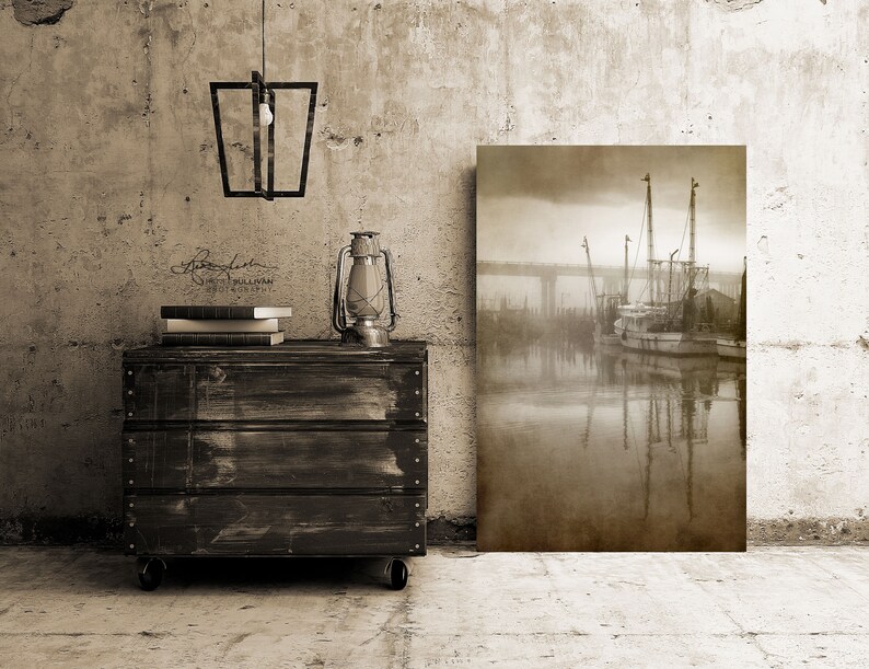 May include: A sepia-toned photograph of a fishing boat docked in a harbor, with a bridge in the background. The boat is surrounded by fog and the water is calm and reflective. The photograph is printed on canvas and mounted on a wooden frame.