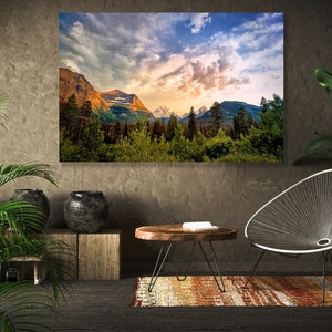 Op de afbeelding: Een woonkamer interieur met een grote ingelijste landschapsfoto van een bergketen met een bewolkte lucht. De foto hangt aan een getextureerde muur. Er is een houten salontafel met een boek erop, een witte draadstoel en twee planten in potten.