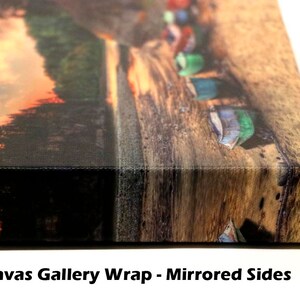 May include: A close-up of the side of a canvas gallery wrap, showing the mirrored edges of the image. The image shows a sunset over a forest with a row of colorful boats on a beach.