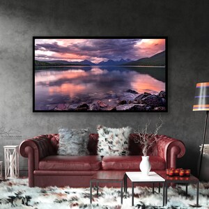 Pu&ograve; includere: Una fotografia incorniciata di un lago di montagna con un tramonto rosa e viola riflesso nell'acqua. Le montagne sono sullo sfondo e ci sono rocce in primo piano.