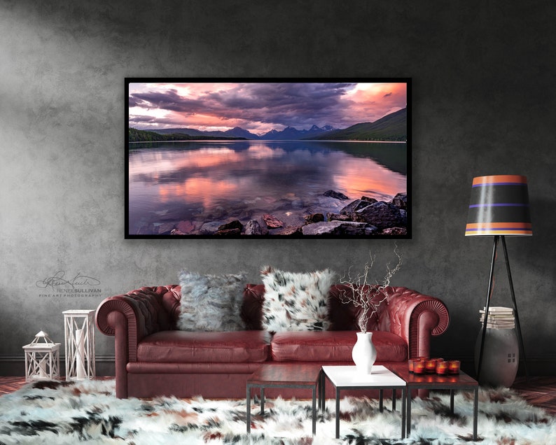 Pu&ograve; includere: Una fotografia incorniciata di un lago di montagna con un tramonto rosa e viola riflesso nell'acqua. Le montagne sono sullo sfondo e ci sono rocce in primo piano.