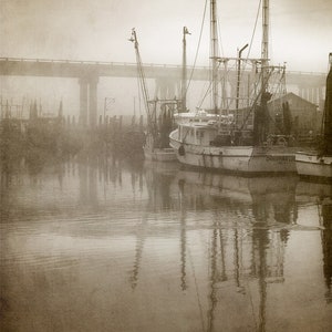 May include: A sepia-toned photograph of three fishing boats docked at a pier in a foggy harbor. The boats are silhouetted against the fog, and the water is calm and reflective. The name of the boat in the foreground is "CHRISTINA L."